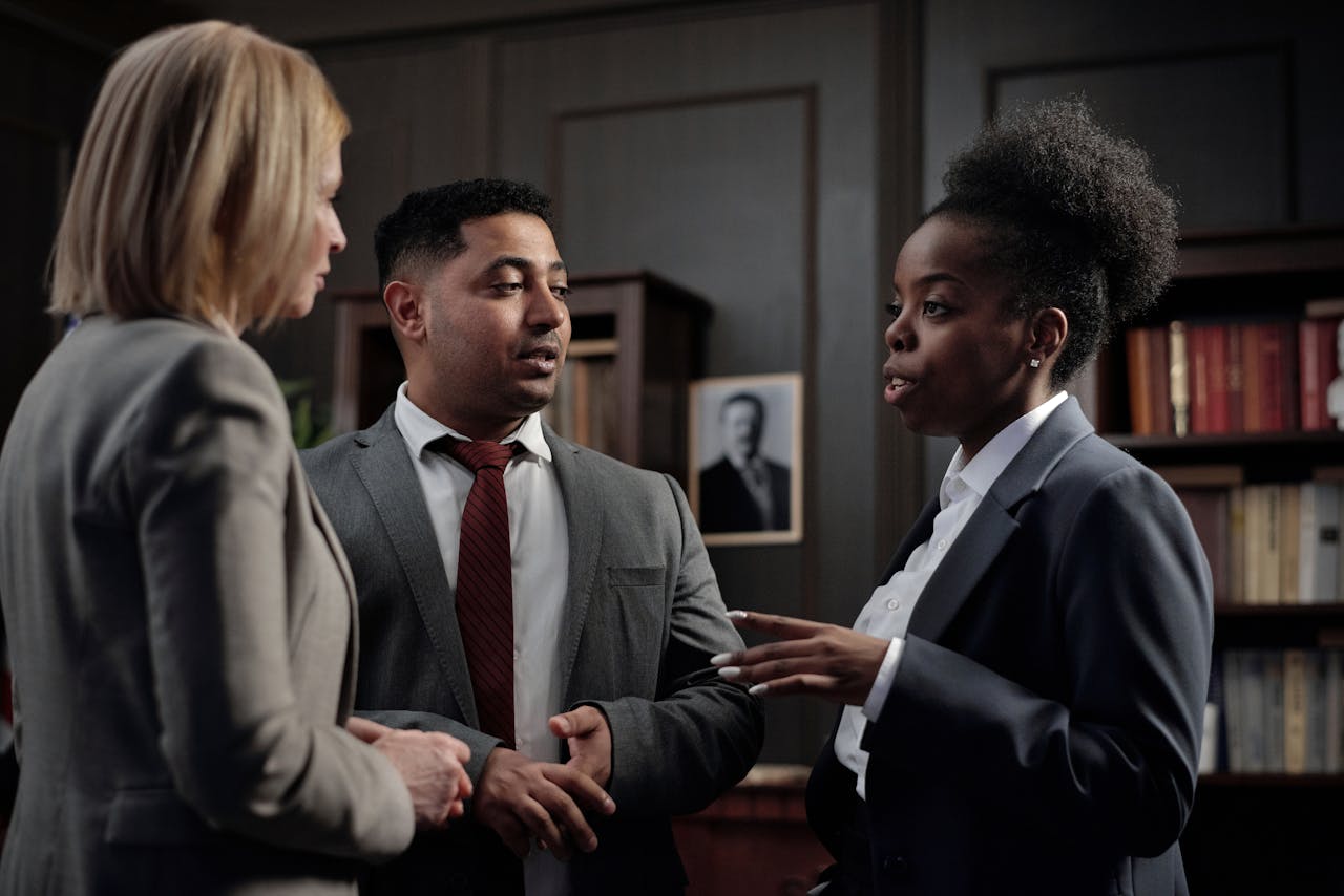 three people in a room, wearing suits discussing business