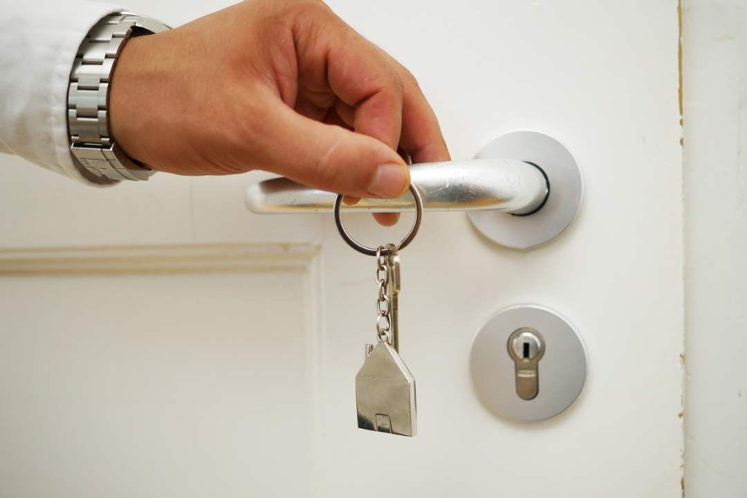 a man holding a key ring in front of a silver door handle